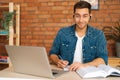 Front view of smiling male student studying online from home using laptop, writing notes, watching video class lesson Royalty Free Stock Photo