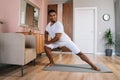 Front view of smiling strong African-American man doing side lunge exercise at home