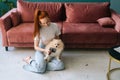 Front view of smiling young woman gently combing pretty white small Spitz pet dog, sitting on floor at home. Royalty Free Stock Photo