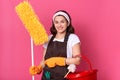 Front view of smiling young woman housewife in casual clothes and apron, doing housework isolated on pink background, holding Royalty Free Stock Photo