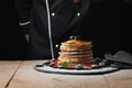 Front view of Stack of homemade plain pancakes with strawberries, blueberries and maple syrup served on black plate on black backg
