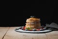 Front view of Stack of homemade plain pancakes with strawberries, blueberries and maple syrup served on black plate on black backg