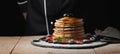 Front view of Stack of homemade plain pancakes with strawberries, blueberries and maple syrup served on black plate on black backg