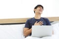 Front view : Surprised happy asian man using Laptop on bed read good news on internet. Royalty Free Stock Photo