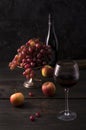 Front view of a tall fruit bowl of red and black grape, apples with wine bottle and goblet with a drink