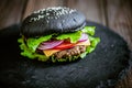 Front view of tasty, appetit black burger with meat cutlet and vegetables on black stone board. Royalty Free Stock Photo