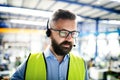 Front view of technician or engineer with headset standing in industrial factory.