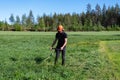 Front view at teenage boy mowing grass with handheld gasoline lawn mower. He wears eye and ear protection headphones. Health and