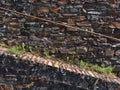 Front view of textured stone wall with ascending path and rusty metal railing with orange patterned bricks and weed in between.