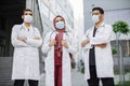 three multiethnic healthcare workers wearing face masks, posing with arms crossed outdoors