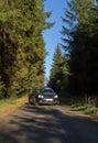 Front view to black car on asphalt road in forest with blue sky