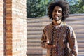 Front view of a cool young smiling afro man using a mobile phone while standing outdoors in a sunny day Royalty Free Stock Photo