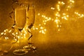 Front view of two glasses of champagne decorated streamers on golden glittering background with defocused lights. Christmas and Royalty Free Stock Photo