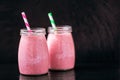 Front view of two jars with yogurt pink smoothie with berries on black background. Selective focus