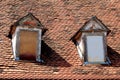 Front view of two old style roof windows closed with wooden boards covered with dilapidated red roof tiles and cracked facade Royalty Free Stock Photo