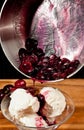 Simmered cherries and syrup poring over a bowel of vanilla ice-cream