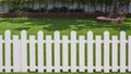 Front view of white wooden fence in front of artificial turf with green plant growing on interlocking brick blocks in front yard Royalty Free Stock Photo