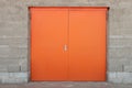 Front view of wide orange or bright red door set in gray stone brick wall with edging.