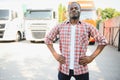 Front view. Young african truck driver is with his vehicle at daytime.