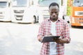 Front view. Young african truck driver is with his vehicle at daytime.