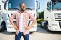 Front view. Young african truck driver is with his vehicle at daytime.