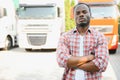 Front view. Young african truck driver is with his vehicle at daytime.