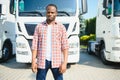 Front view. Young african truck driver is with his vehicle at daytime.