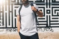 Front view. Young bearded millennial man dressed in white t-shirt is stands against brick wall. Mock up.