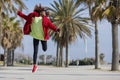 Front view of young beautiful curly african american woman jumping and dancing while listening music and smiling outdoors Royalty Free Stock Photo