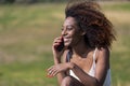 Front view of young beautiful curly smiling woman sitting on ground in a city park while using a mobile phone outdoors Royalty Free Stock Photo