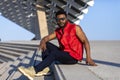 Front view of young black man wearing sunglasses sitting on staircase in a sunny day while looking camera Royalty Free Stock Photo