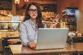 Front view. Young businesswoman is sitting in cafe working on laptop. Girl blogging, learning online, checking email.