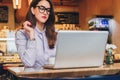 Front view. Young businesswoman is sitting in cafe working on laptop. Girl blogging, learning online, checking email.