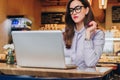 Front view. Young businesswoman is sitting in cafe working on laptop. Girl blogging, learning online, checking email.