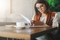 Front view.Young businesswoman is sitting in coffee shop at table,reading documents.Student is studying online