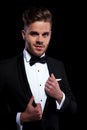 Young elegant man puliing his tuxedo`s collars while looking away Royalty Free Stock Photo