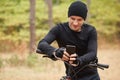 Front view of young European rider standing in forest around trees, holding mobile phone, using online application for searching Royalty Free Stock Photo