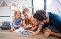 Young family with two small children indoors in bedroom reading a book. Royalty Free Stock Photo