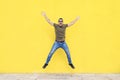 Front view of a young man wearing sunglasses jumping against a yellow bright wall in a sunny day Royalty Free Stock Photo