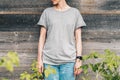 Front view. Young millennial woman dressed in gray t-shirt is stands against gray wood wall.