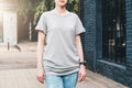 Front view. Young millennial woman dressed in gray t-shirt is stands on city street. Mock up. Royalty Free Stock Photo