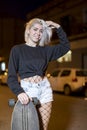 Front view of a young pretty woman looking camera in shorts while standing on the street holding a skateboard at night in the city Royalty Free Stock Photo