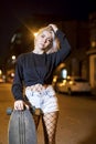 Front view of young pretty woman looking camera in shorts while standing on the street holding a skateboard at night in the city Royalty Free Stock Photo