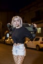 Young pretty woman looking camera in shorts while standing on the street holding a skateboard at night in the city Royalty Free Stock Photo