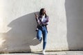 Front view of a young smiling african american woman standing outdoors while smiling and listening music by earphones in a sunny Royalty Free Stock Photo