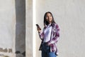 Front view of a young smiling african american woman standing outdoors while smiling and listening music by earphones in a sunny Royalty Free Stock Photo