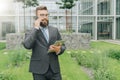 Young smiling businessman in suit and tie is standing outdoor,holding tablet computer and talking on his cell phone Royalty Free Stock Photo