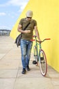 Front view of a young trendy man with a fixed bike wearing casual clothes while using a mobile phone against a yellow wall Royalty Free Stock Photo