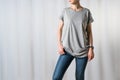 Front view of young woman, dressed in a gray T-shirt and blue jeans, standing on light gray background Royalty Free Stock Photo