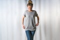 Front view of young woman,dressed in gray t-shirt and blue jeans, standing in studio for light background Royalty Free Stock Photo